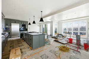 Kitchen featuring a center island with sink, appliances with stainless steel finishes, gray cabinets, pendant lighting, and a tray ceiling