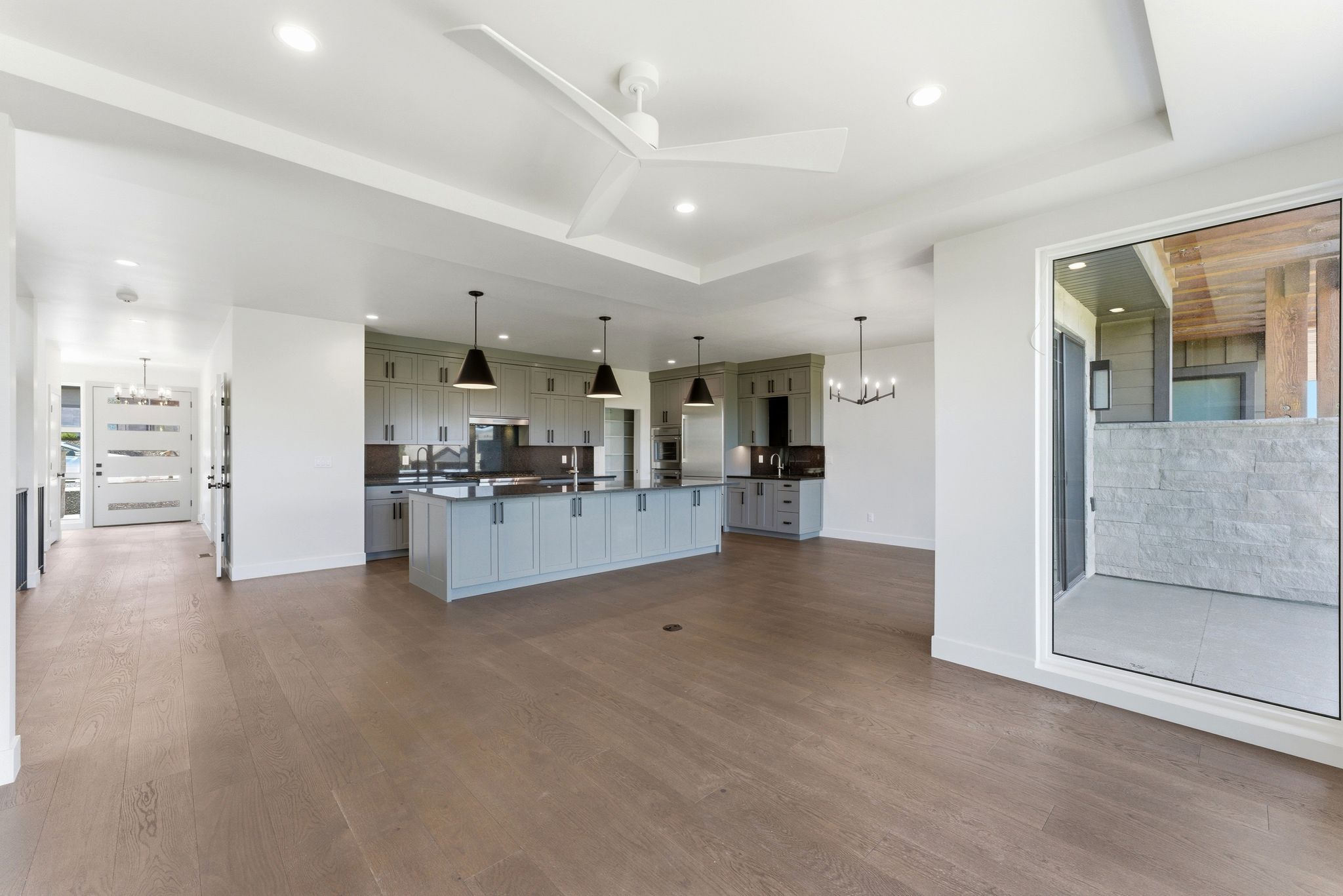 Spacious interior featuring wide plank wood-finish flooring, a contemporary kitchen with light gray cabinetry and dark countertops, and an expansive kitchen island with pendant lighting