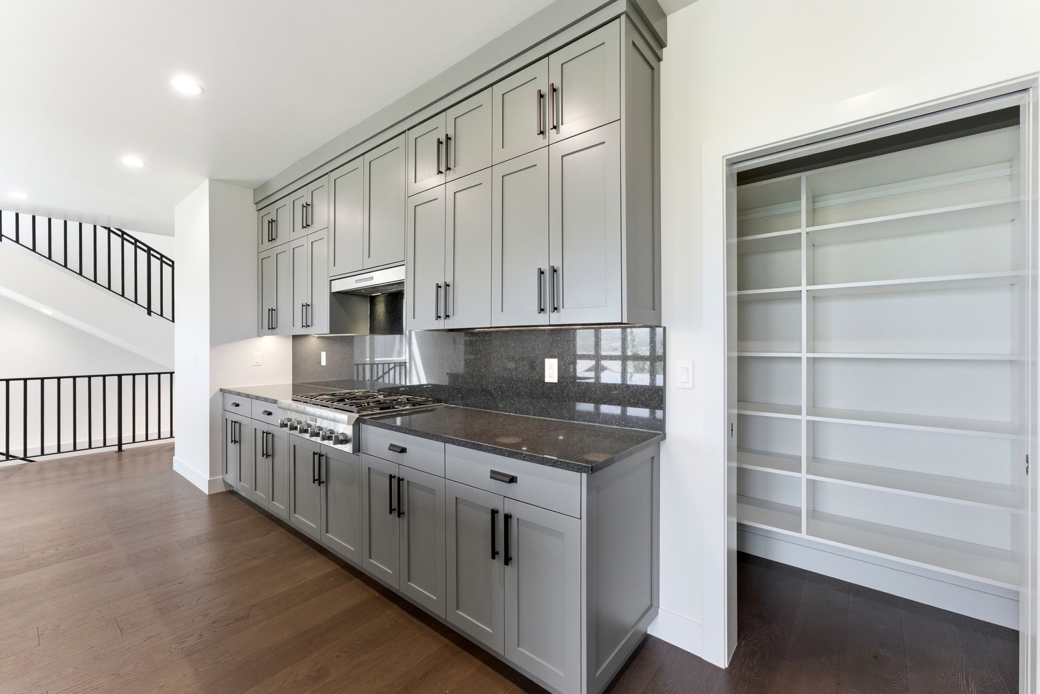 Kitchen featuring extensive gray cabinetry with black hardware, dark stone countertops, a gas range with a stainless steel hood, and a built-in pantry with shelving