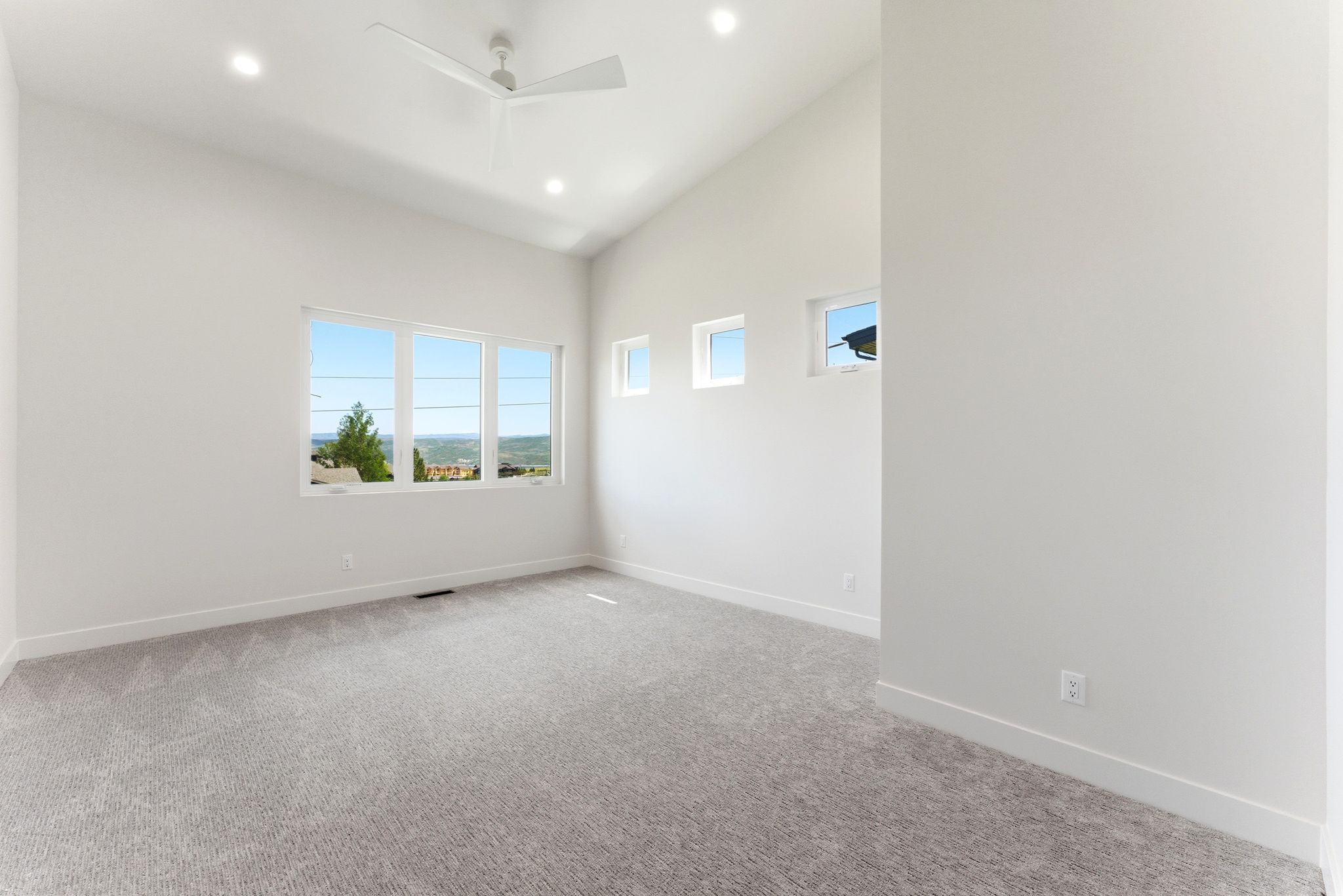 Spacious room featuring vaulted ceilings, recessed lighting, a modern ceiling fan, gray patterned carpet, and multiple windows
