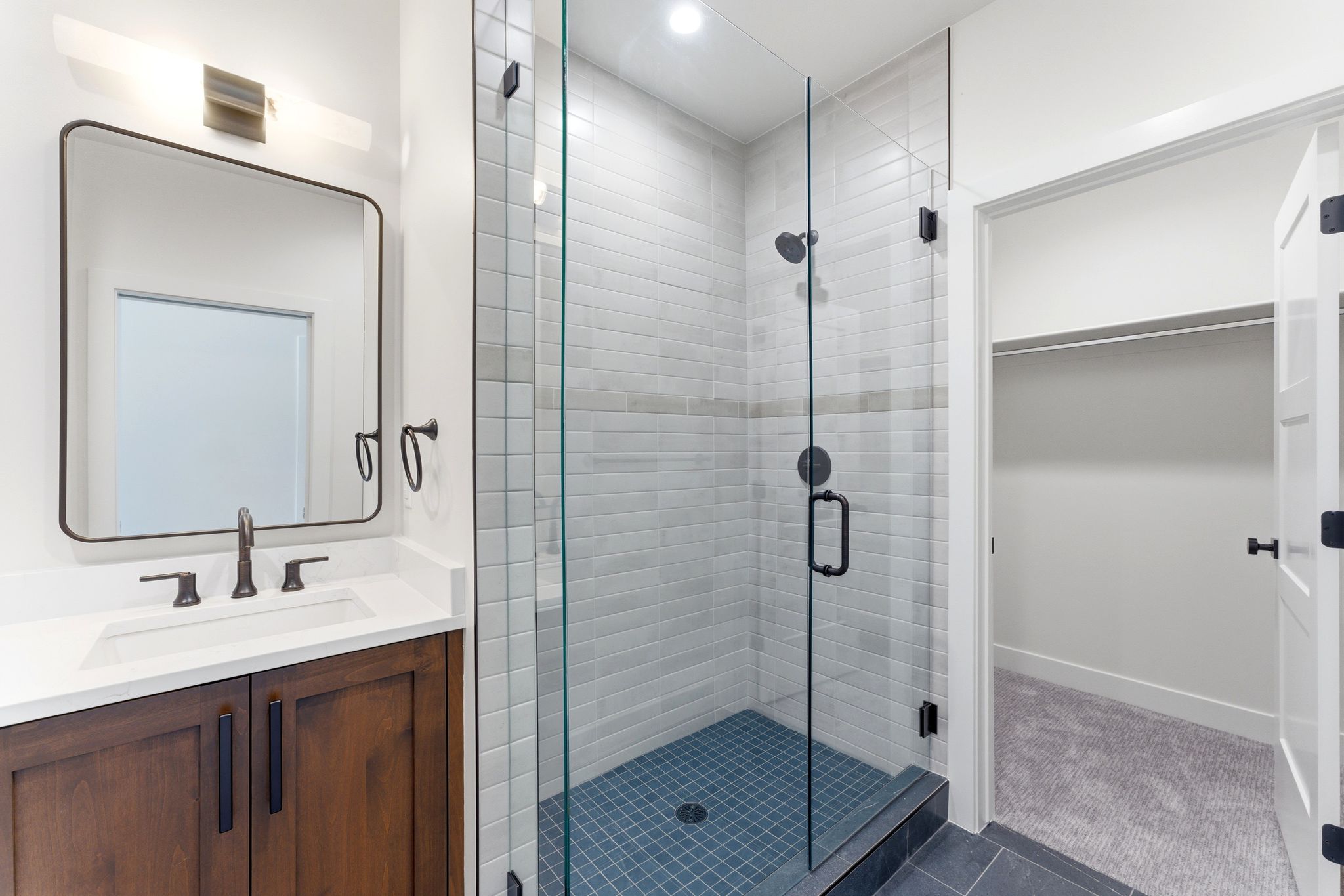 Modern bathroom featuring a glass-enclosed shower with subway tile surround and dark tile flooring, a wood-finish vanity with a white countertop and integrated sink, and an elegant framed mirror