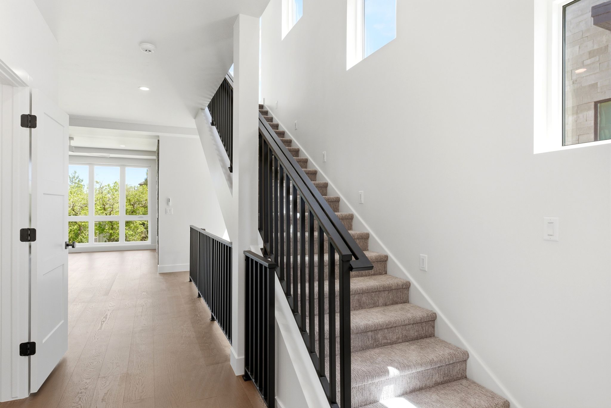 Modern interior staircase with black metal balusters and carpeted treads, complemented by light wood-finish flooring