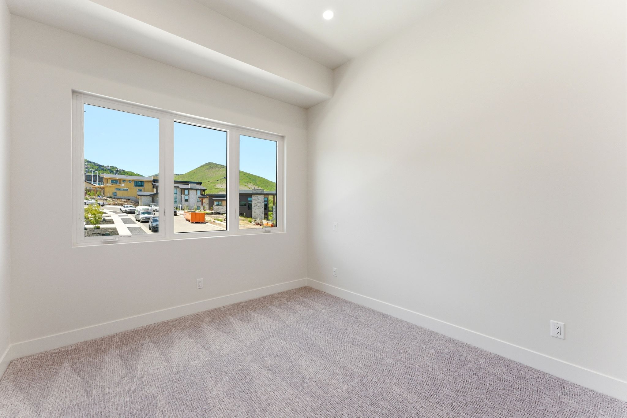 Bright room featuring a multi-pane window, neutral-toned walls, recessed lighting, patterned carpeting, and white baseboards