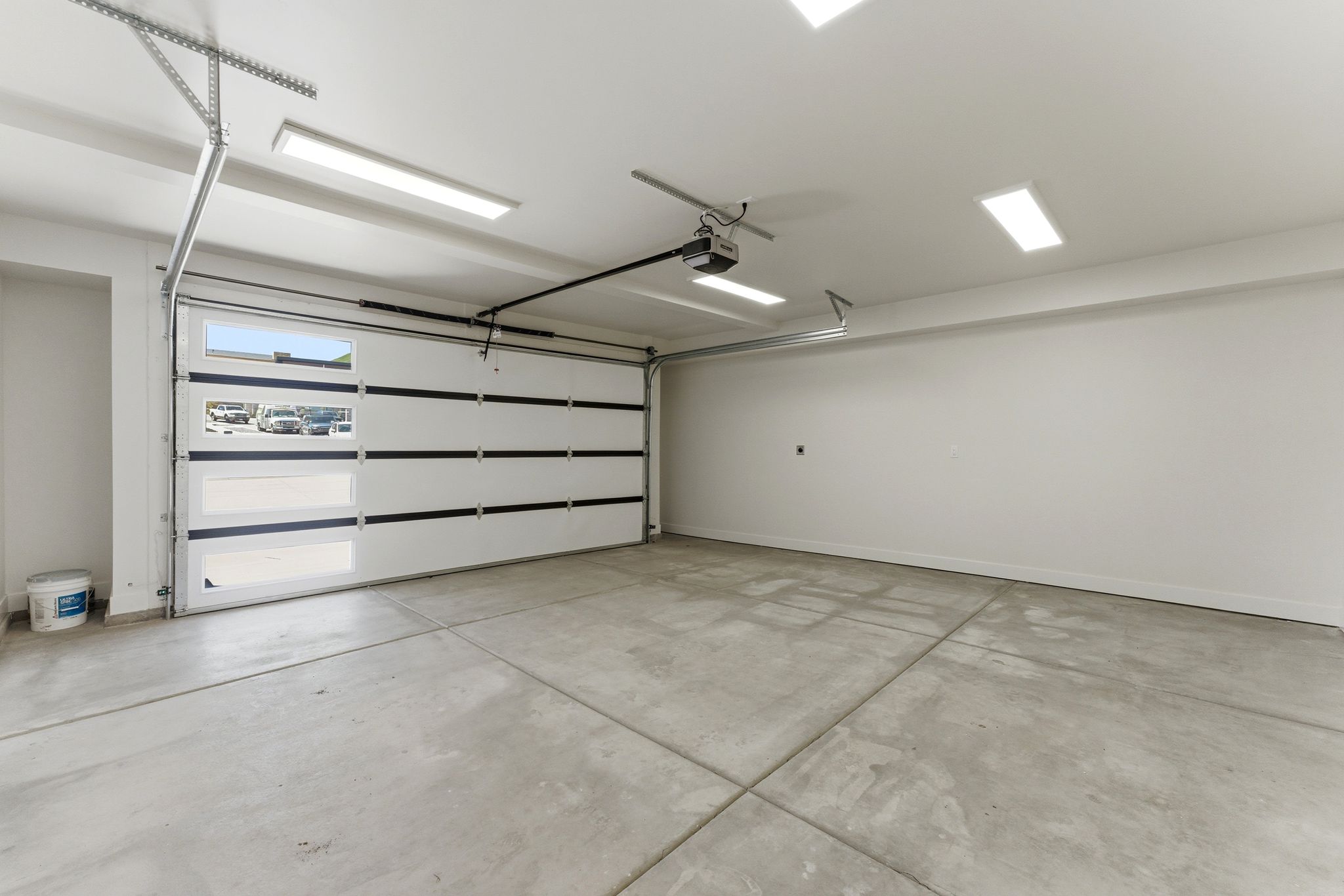 Spacious garage featuring a sectional door with frosted glass panels, concrete flooring, and multiple overhead recessed light fixtures