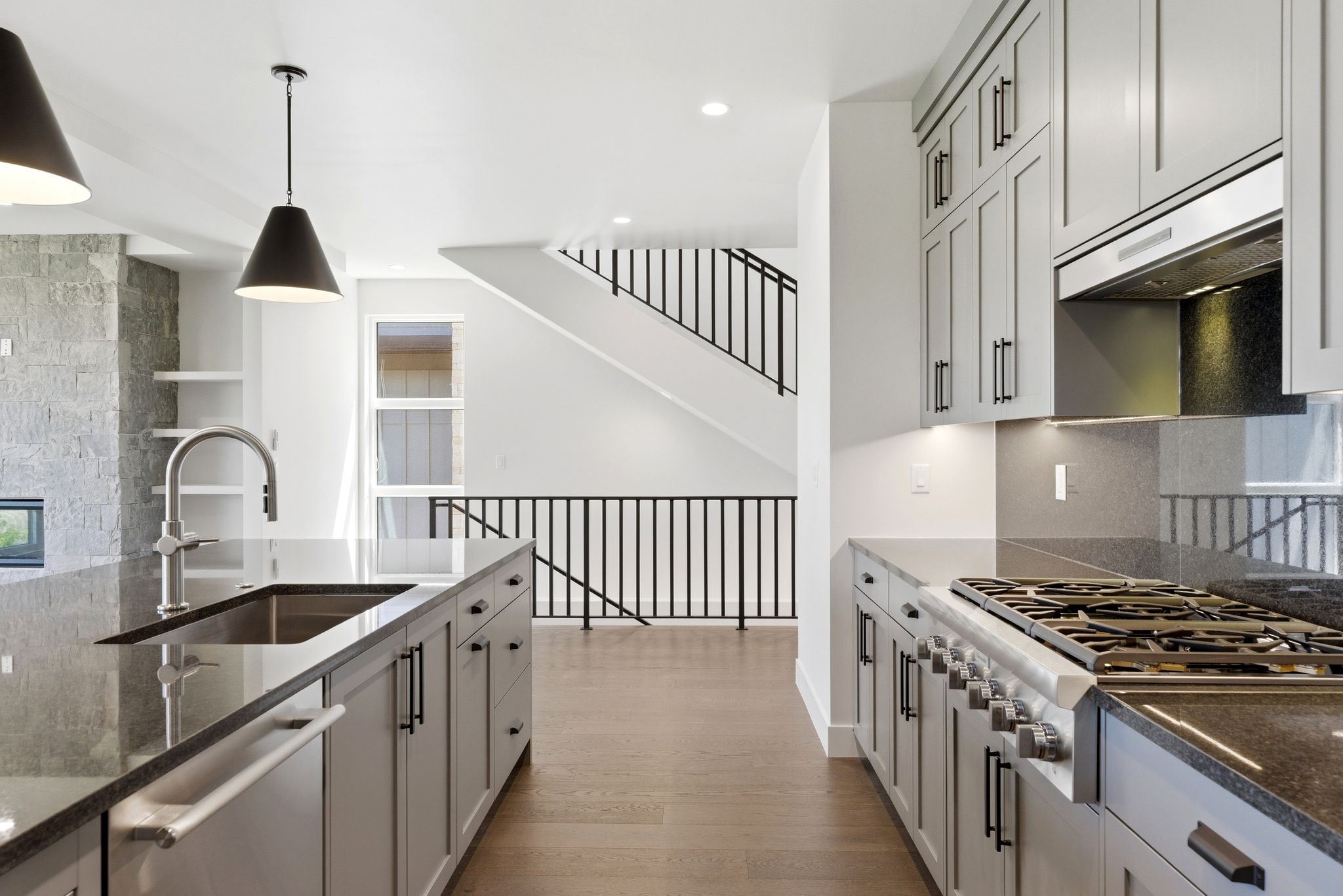 Spacious kitchen featuring an expansive island with an undermount sink, pendant lighting, professional-grade range with hood, extensive cabinetry, and wood-finish flooring