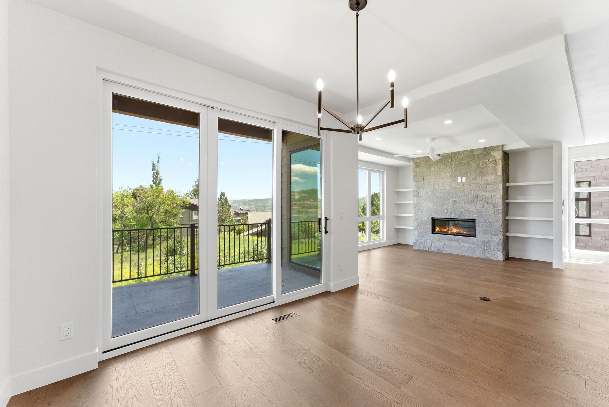Spacious living area featuring wood-finish flooring, a stone-clad fireplace, integrated shelving, and a modern chandelier