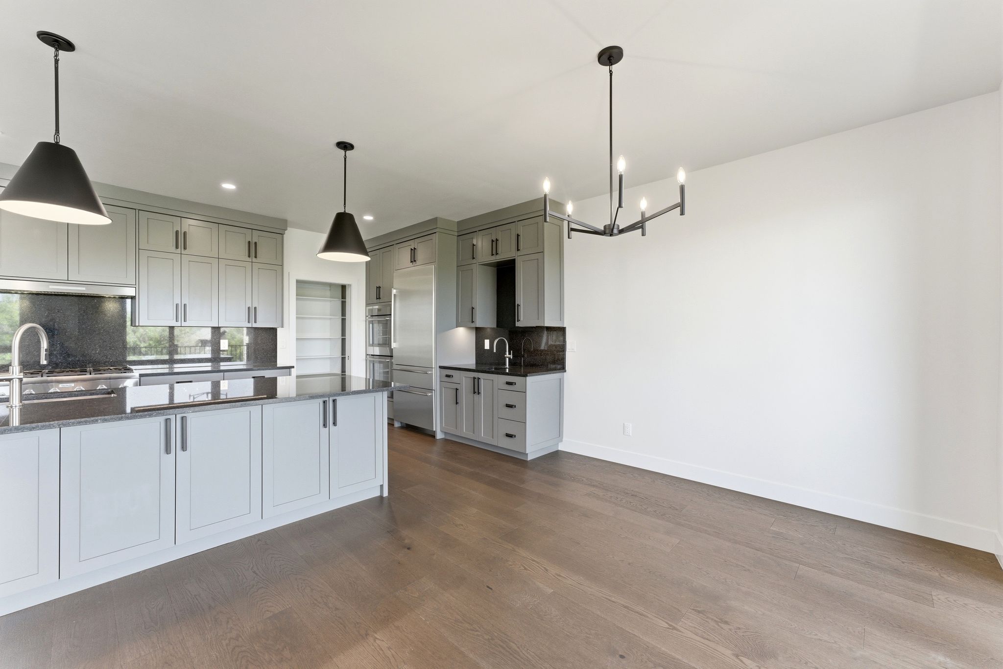 Contemporary kitchen featuring light gray cabinetry, dark stone countertops, stainless steel appliances, and wood-finish flooring