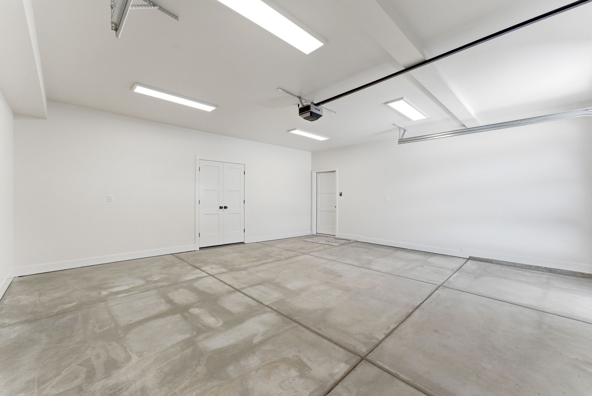 Spacious garage featuring a concrete floor, bright overhead lighting, painted walls, and multiple access doors