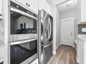 Kitchen with wood finished floors, stainless steel appliances, white cabinets, backsplash, and visible vents