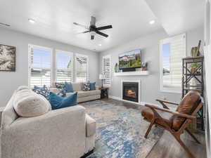 Living room with a glass covered fireplace, wood finished floors, baseboards, and ceiling fan