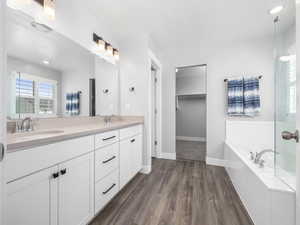 Full bath with a garden tub, wood finished floors, a sink, and double vanity