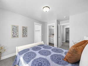Bedroom featuring ensuite bath, baseboards, a walk in closet, and carpet flooring