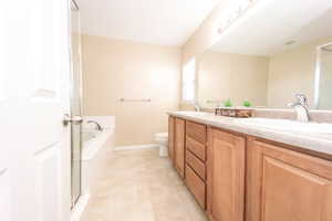 Bathroom attached to the primary suite, featuring a garden tub, a sink, a double vanity, and a toilet.