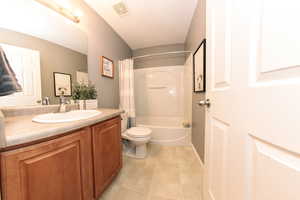 Bathroom featuring a shower/bath combination with curtain, toilet, vanity, and a full bath with tile flooring