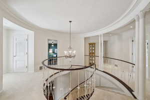 Hallway featuring carpet, visible vents, an inviting chandelier, and an upstairs landing