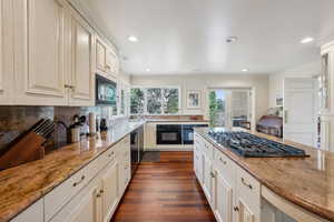 Kitchen with light stone counters, tasteful backsplash, crown molding, black appliances, and dark wood-style floors