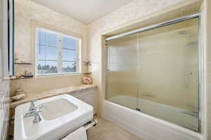 Full bath with bath / shower combo with glass door, a sink, and wallpapered walls