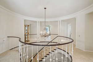 Staircase with an inviting chandelier, baseboards, carpet floors, and crown molding