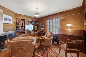 Sitting room with a high end fireplace, wood walls, ornamental molding, and built in features