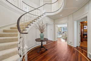 Entrance foyer with wood finished floors, a high ceiling, stairway, a decorative wall, and ornamental molding