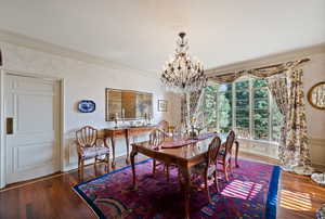 Dining space with ornamental molding, a chandelier, wood finished floors, and a wainscoted wall