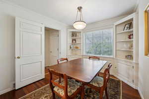 Dining space with built in shelves, visible vents, crown molding, and dark wood-style floors
