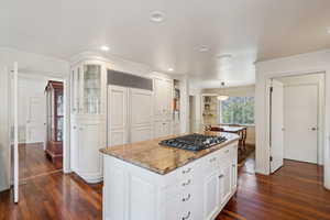 Kitchen with stainless steel gas cooktop, white cabinets, dark wood-style flooring, and crown molding