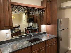 Kitchen featuring brown cabinets, dark stone countertops, a wall unit AC, a sink, and appliances with stainless steel finishes