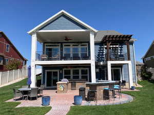 Back of house with a ceiling fan, a balcony, outdoor dry bar, and a yard