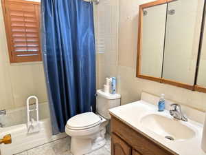 Full bath featuring tile patterned floors, toilet, vanity, tile walls, and shower / bath combo with shower curtain