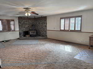 Unfurnished living room with carpet, a wood stove, a ceiling fan, and a wealth of natural light