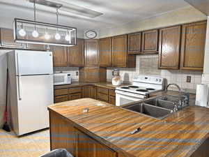 Kitchen with a sink, tasteful backsplash, white appliances, pendant lighting, and butcher block counters