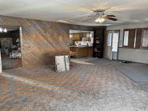 Interior space featuring wooden walls, carpet flooring, open floor plan, and a ceiling fan