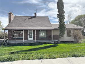View of front of house featuring a porch, a front lawn, roof with shingles, and brick siding