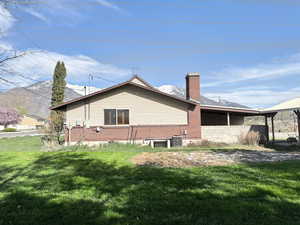 Rear view of property with central AC, a mountain view, a chimney, and a lawn