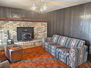 Living room with carpet floors, a wood stove, wood walls, and a notable chandelier