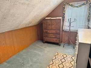 Additional living space featuring lofted ceiling, wooden walls, and carpet flooring