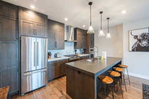 Kitchen with wall chimney range hood, dark countertops, light wood-style flooring, a kitchen bar, and appliances with stainless steel finishes