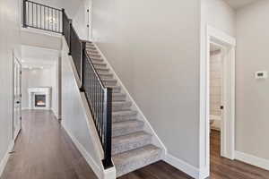 Stairway with baseboards, a lit fireplace, a high ceiling, and wood finished floors