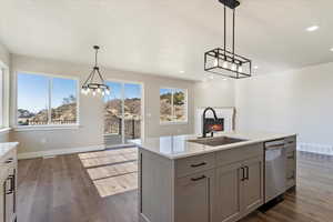 Kitchen featuring light countertops, a sink, a chandelier, stainless steel dishwasher, and dark wood-type flooring