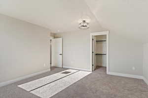 Unfurnished bedroom featuring light carpet, a walk in closet, a textured ceiling, lofted ceiling, and baseboards