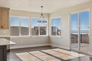 Unfurnished dining area featuring dark wood finished floors, baseboards, a notable chandelier, and a textured ceiling