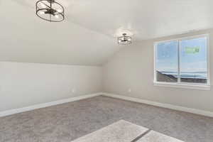 Additional living space featuring a notable chandelier, carpet flooring, lofted ceiling, baseboards, and visible vents