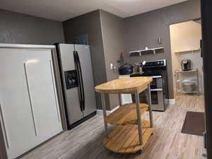 Kitchen featuring baseboards, a textured wall, light wood-style flooring, and stainless steel appliances