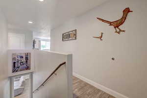 Corridor featuring baseboards, an upstairs landing, light wood finished floors, and recessed lighting