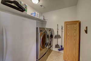 Washroom featuring washing machine and clothes dryer, light tile patterned flooring, visible vents, and laundry area