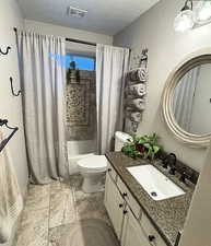 Full bathroom with a textured ceiling, toilet, visible vents, shower / bath combo with shower curtain, and vanity