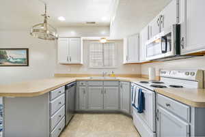 Kitchen featuring stainless steel appliances, a peninsula, a sink, and gray cabinets