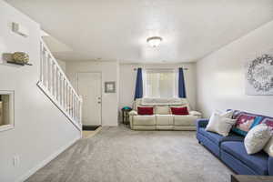 Carpeted living room featuring baseboards, a textured ceiling, and stairs