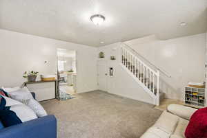 Carpeted living room featuring a notable chandelier, baseboards, a textured ceiling, and stairs